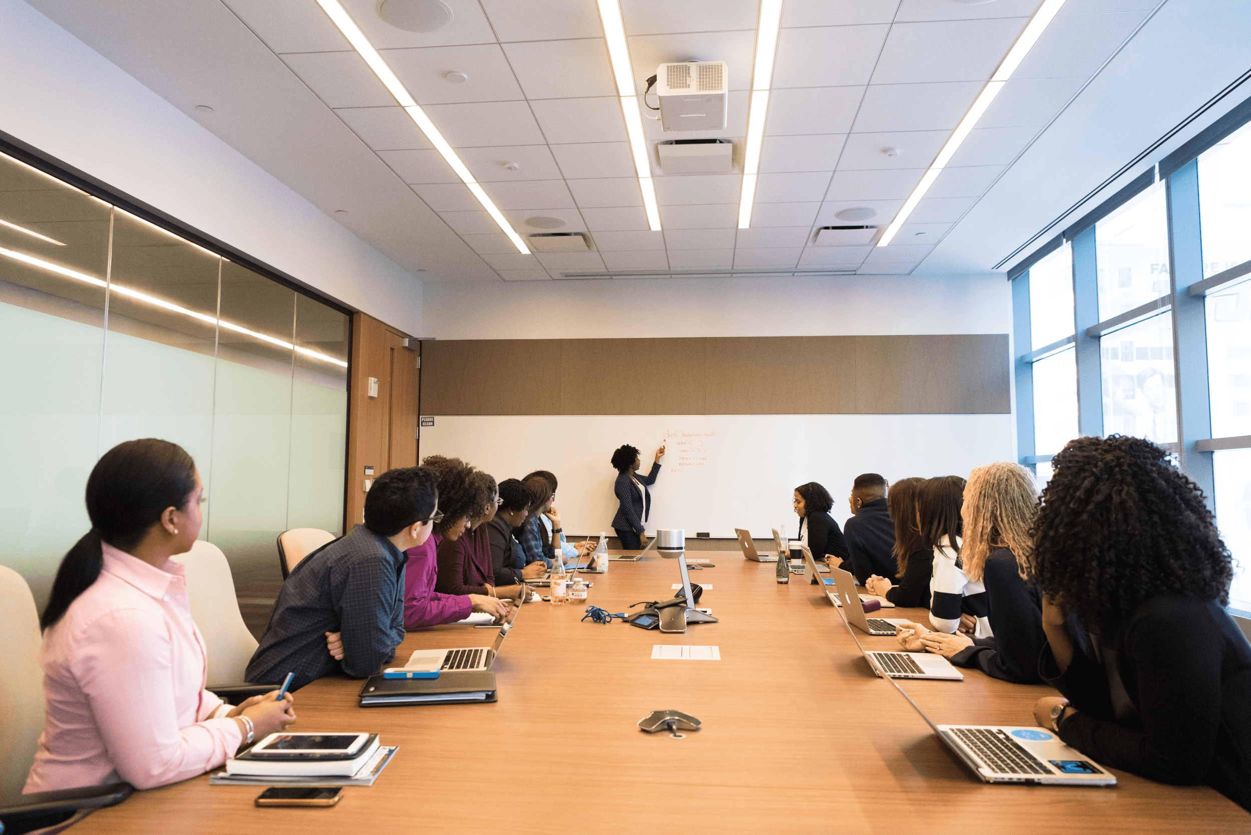 group of people seated at table looking at woman at whiteboard